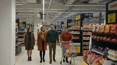 Skupina lidí nakupuje v supermarketu mezi regály se zbožím a vozíkem